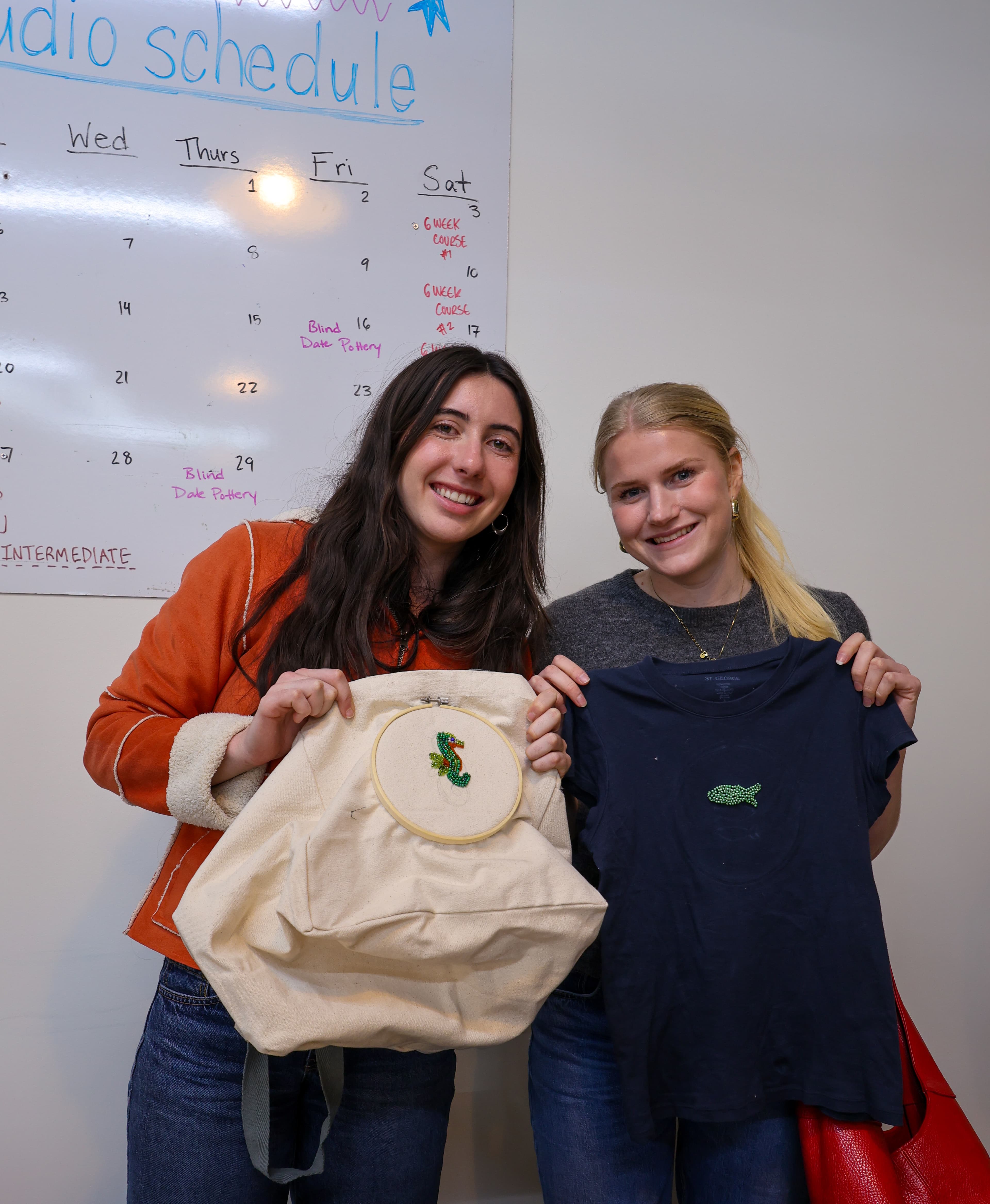 Two students proudly showing a beaded seahorse tote bag and fish t-shirt