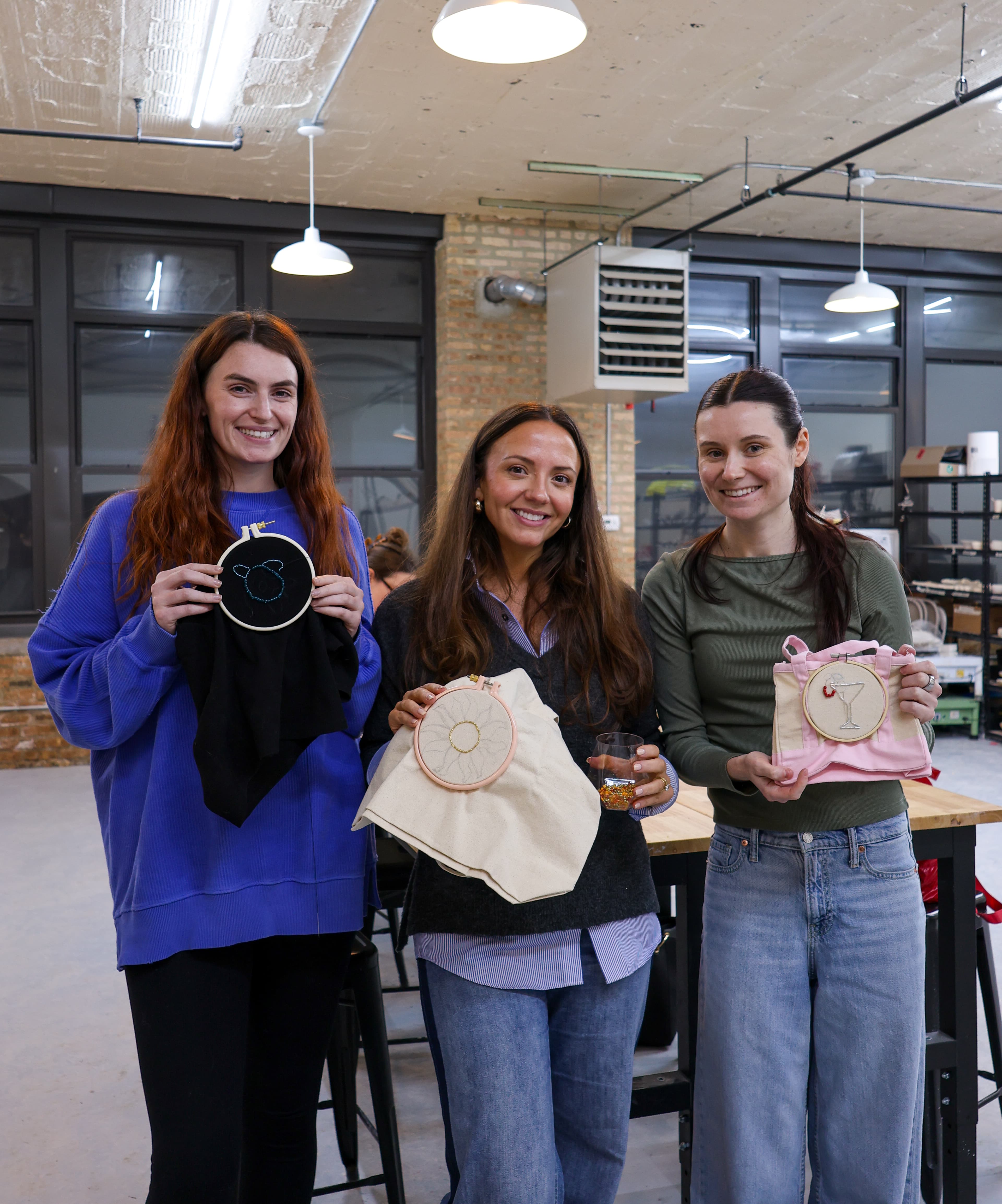 Three students holding their finished beaded embroidery pieces in hoops